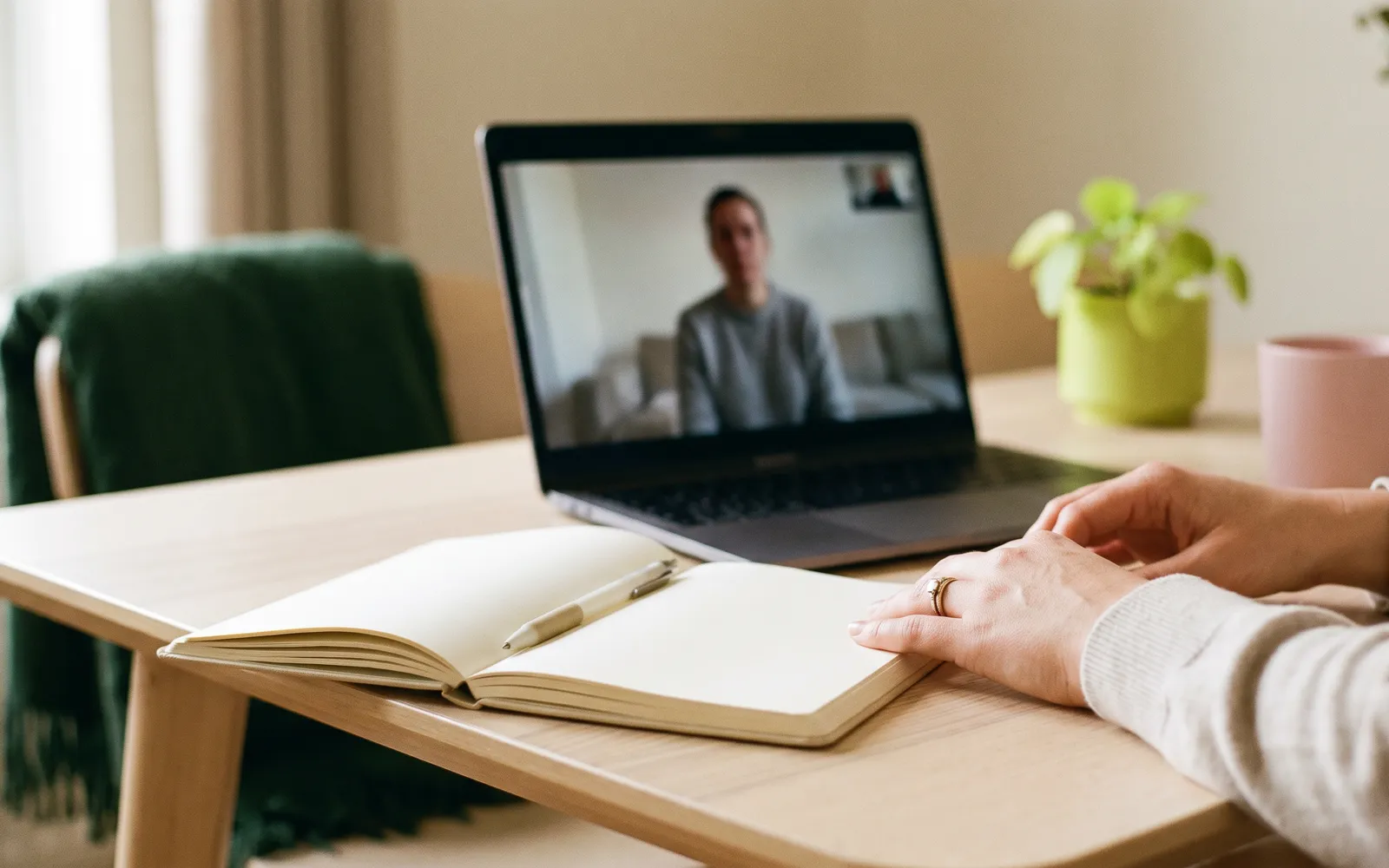 Hands resting on an open notebook beside a laptop during a call.