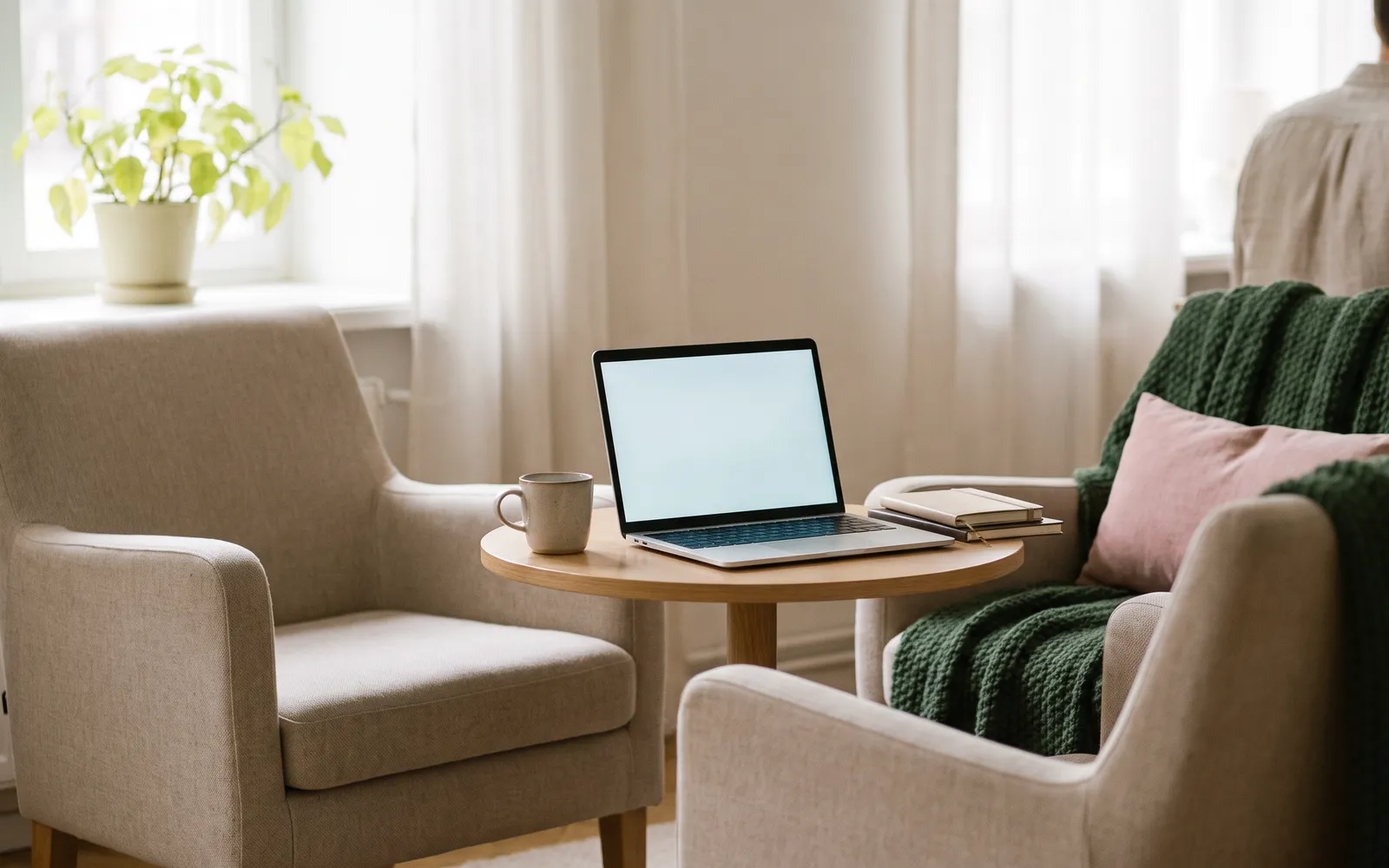 Two armchairs by a small table with an open laptop in a bright room.
